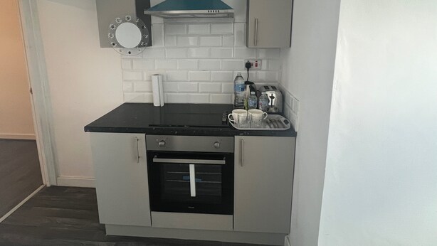 A compact kitchen with a black countertop, a built-in oven, a toaster, and a water dispenser.