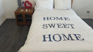 A bed with a white bedspread that reads "HOME SWEET HOME" in large letters.