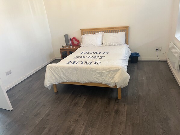 A bedroom with a bed, wooden headboard, white bedding, a bedside table with a lamp, and a nightstand.