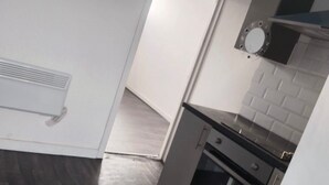 A kitchen with a dark wooden floor, a built-in oven, and a white wall with a vent.