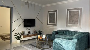Ein Wohnzimmer mit einem türkisfarbenen Sofa, einem Flachbildfernseher, einem Couchtisch und Dekorationselementen.