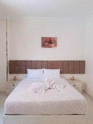 A neatly made bed with a towel art arrangement, a headboard, and a wall-mounted artwork.