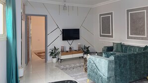Ein Wohnzimmer mit Flachbildfernseher an der Wand, einem grünen Sofa, einer Holzkommode und einem gemusterten Teppich.