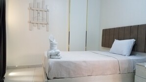 Ein ordentlich bezogenes Bett mit weißer Decke, einem Holzkopfteil und einem kleinen Nachttisch mit Schubladen.