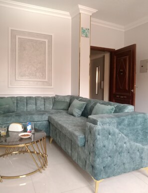 A living room with a sectional sofa, a glass coffee table, and a door.