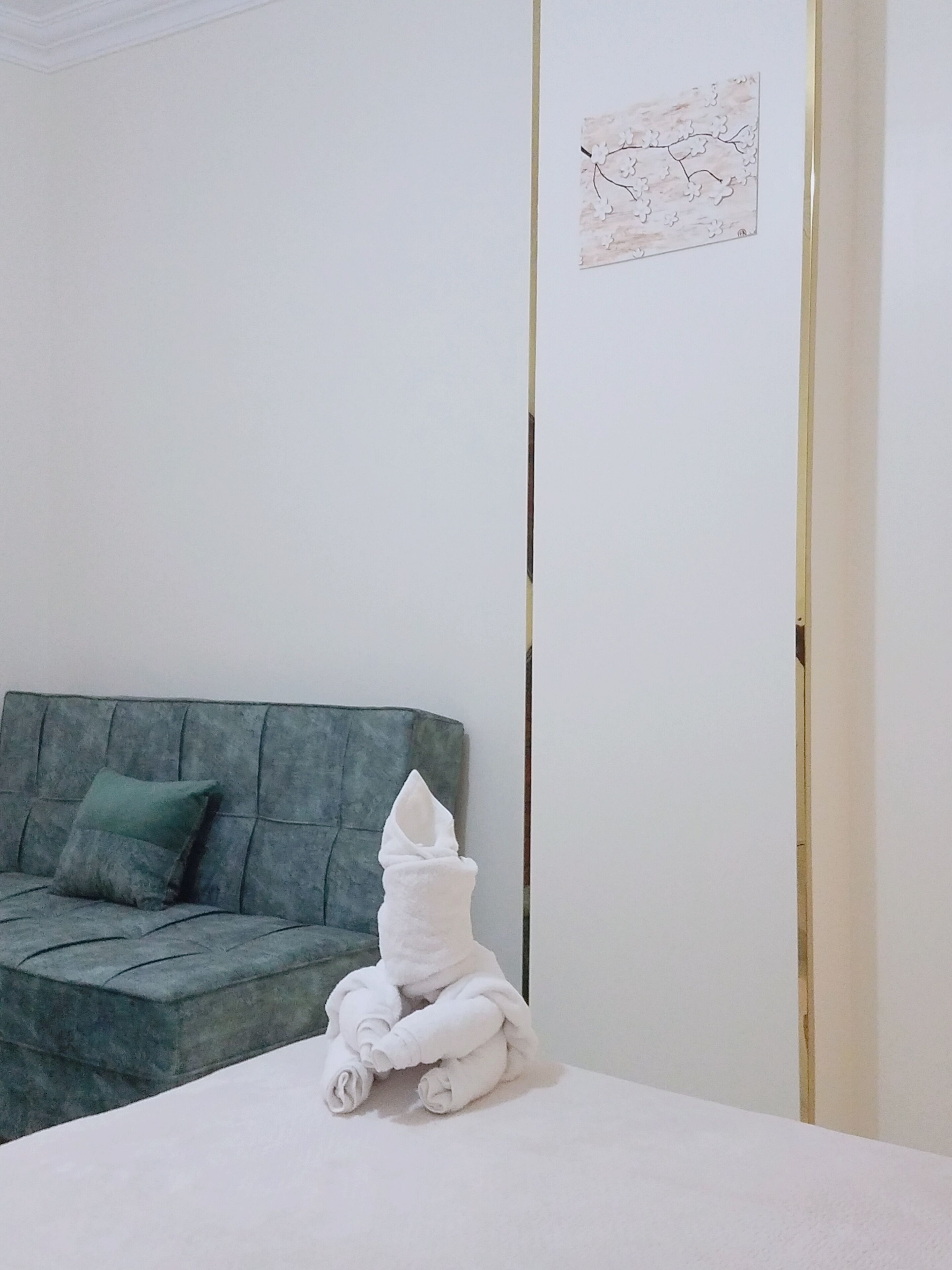 Una habitación con una cama, un sofá verde y una obra de arte colgada en la pared.