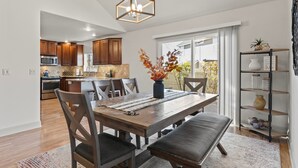 A modern kitchen with wooden cabinets, a built-in oven, and a dining area with a wooden table and chairs. - Spacious Getaway, Perfect for Groups, Fire pit, BBQ, 70" TV, near The Village, TopGolf, Parks (Meridian)