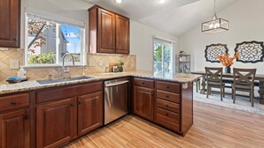 A kitchen with wooden cabinets, a stainless steel dishwasher, and a granite countertop. - Spacious Getaway, Perfect for Groups, Fire pit, BBQ, 70" TV, near The Village, TopGolf, Parks (Meridian)