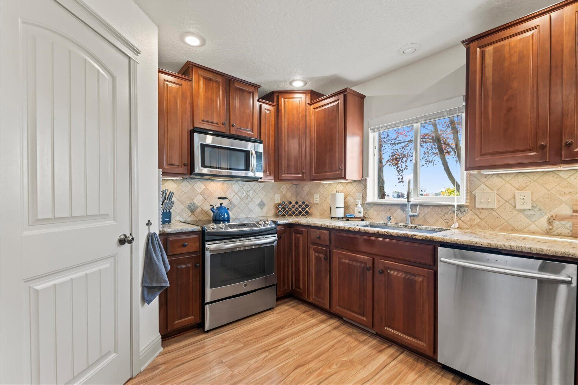 A kitchen with wooden cabinets, stainless steel appliances, a window with a view, and a tiled backsplash.