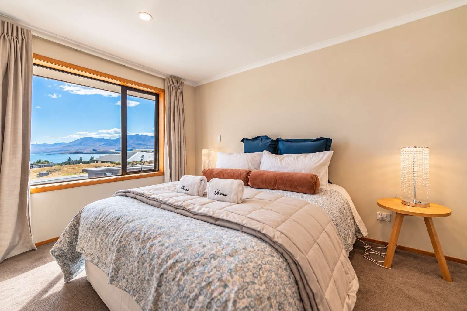 A hotel room with a large bed, a bedside table with a lamp, and a window offering a view of the outdoors.