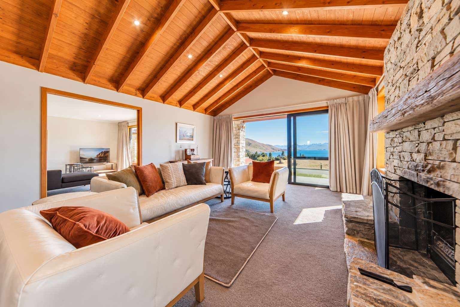 A spacious living room with a stone fireplace, a large window offering a view of the outdoors, and a cozy seating area with a sofa and armchairs.