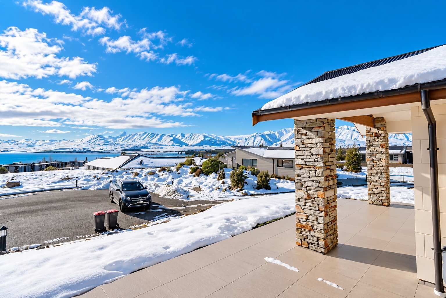 A modern building with stone pillars, a covered entrance, and a view of snow-covered mountains and a lake.