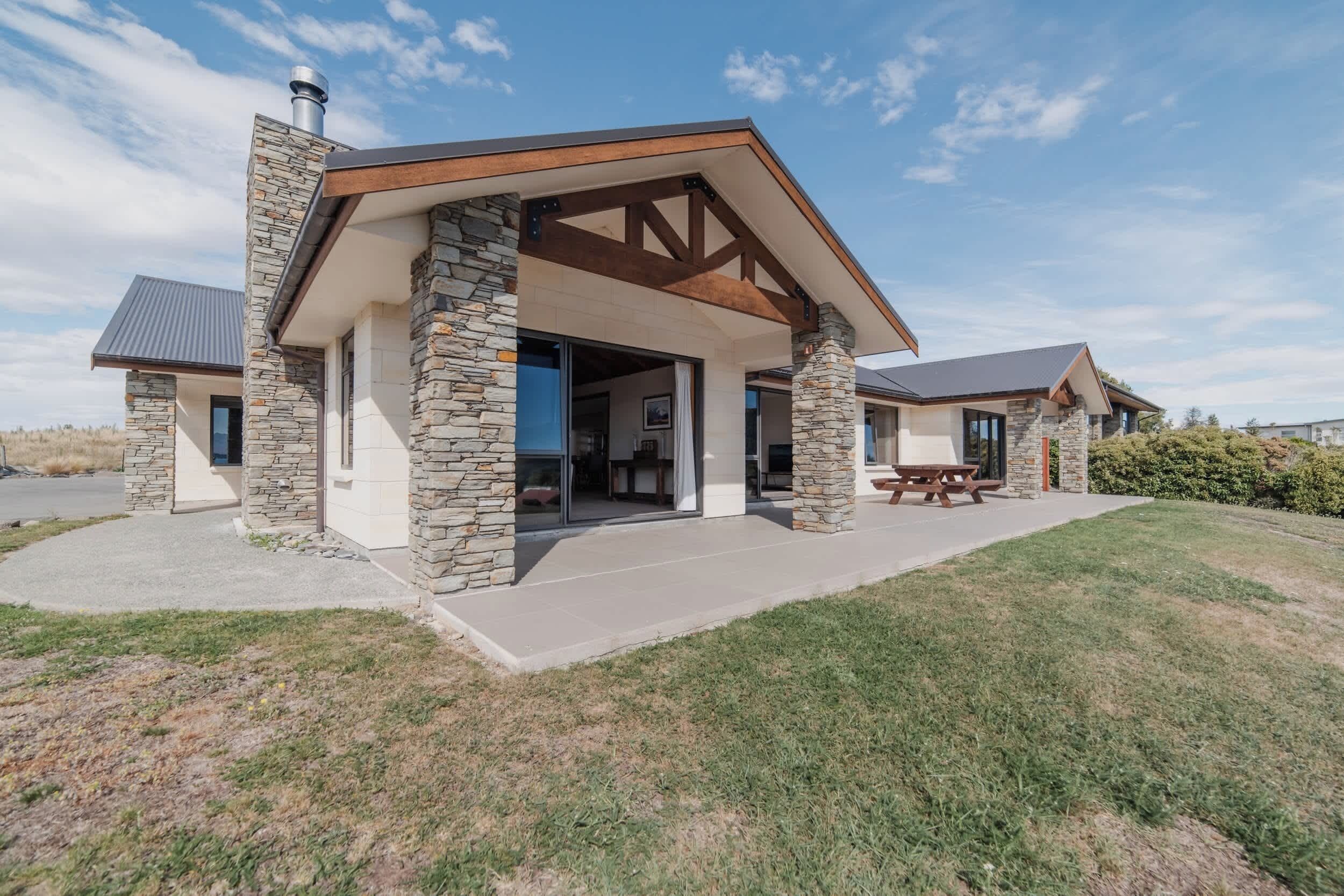 A modern house with stone exterior walls, a covered porch, and a visible interior with a dining area.