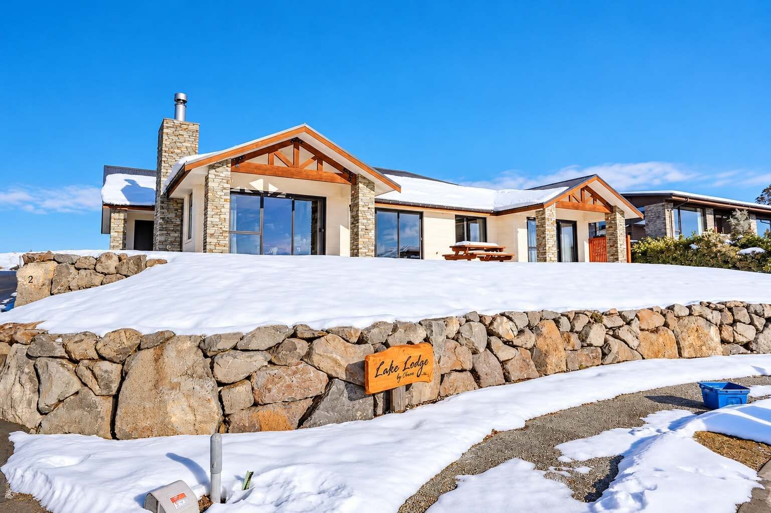 A stone-walled lodge with a clear sky, a sign reading 'Lake Lodge,' and a snow-covered ground.