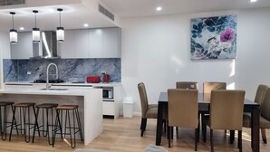 A modern kitchen with a central island, bar stools, and a dining area with chairs and a table. - Brand new House in Sunshine West (Sunshine West)