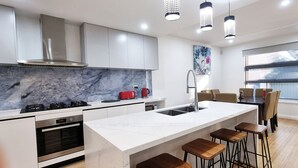A modern kitchen with a marble countertop, stainless steel appliances, and bar stools. - Brand new House in Sunshine West (Sunshine West)