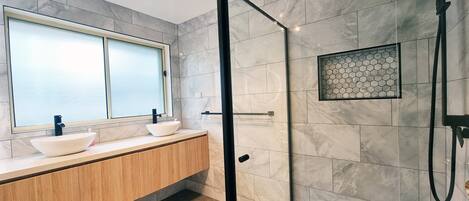 A modern bathroom with a glass-enclosed shower, a large window, and a wooden vanity.