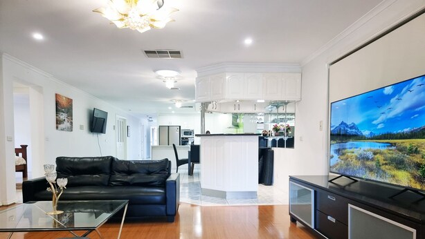 A modern living room with a black leather sofa, a glass coffee table, and a flat-screen TV on a stand. - 5 Bedrooms Spacious Home (Sunshine West)
