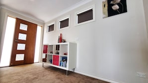 A hallway with a white wall, a wooden door, a white storage unit with red and blue drawers, and a small window with a flower decoration. - St Albans House - Spacious and Modern Home (St. Albans)