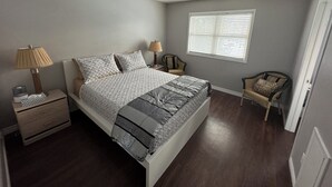 Un dormitorio con una cama, mesitas de noche, una lámpara, una silla y una ventana con persianas.