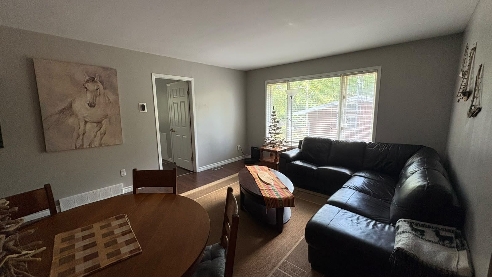 Un salon avec un canapé en cuir noir, une table à manger en bois avec des chaises, une table basse et un tableau accroché au mur.