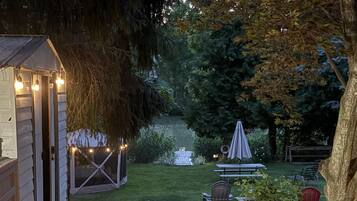 A wooden deck leading to a covered outdoor seating area with string lights, surrounded by trees and a small garden.
