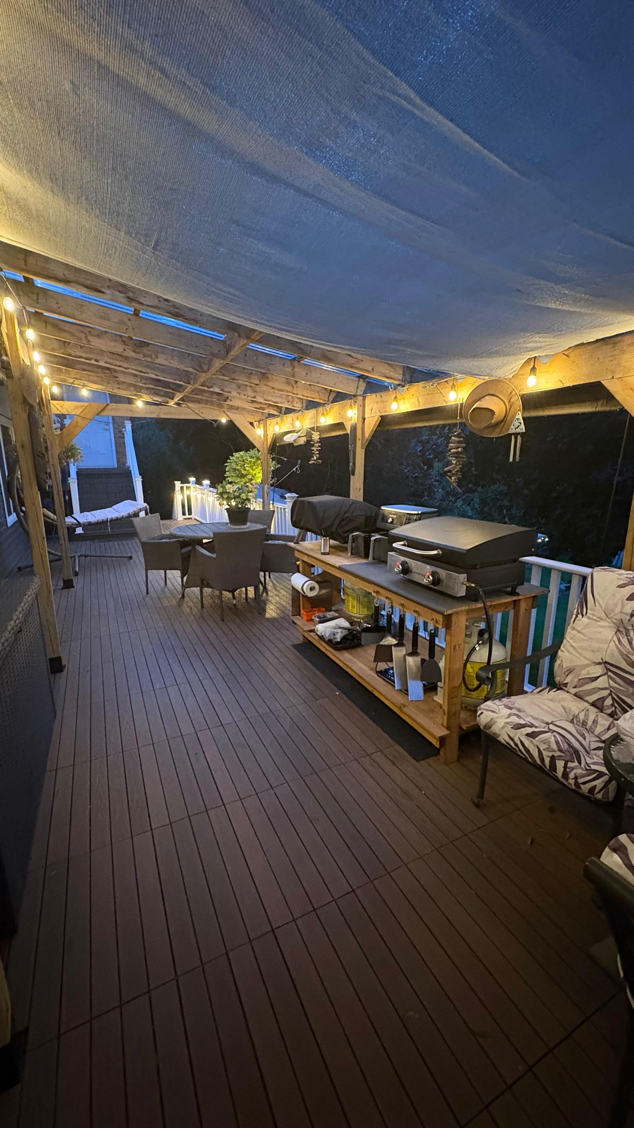 En udendørs terrasse med grillområde, siddepladser og lyskæder.