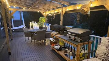 En udendørs terrasse med grillområde, siddepladser og lyskæder.