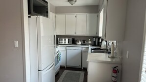 Una cocina compacta con armarios blancos, microondas, tostadora, lavavajillas y un lavamanos pequeño.