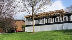 Un patio trasero con césped, un pérgola de madera y un edificio de ladrillo.