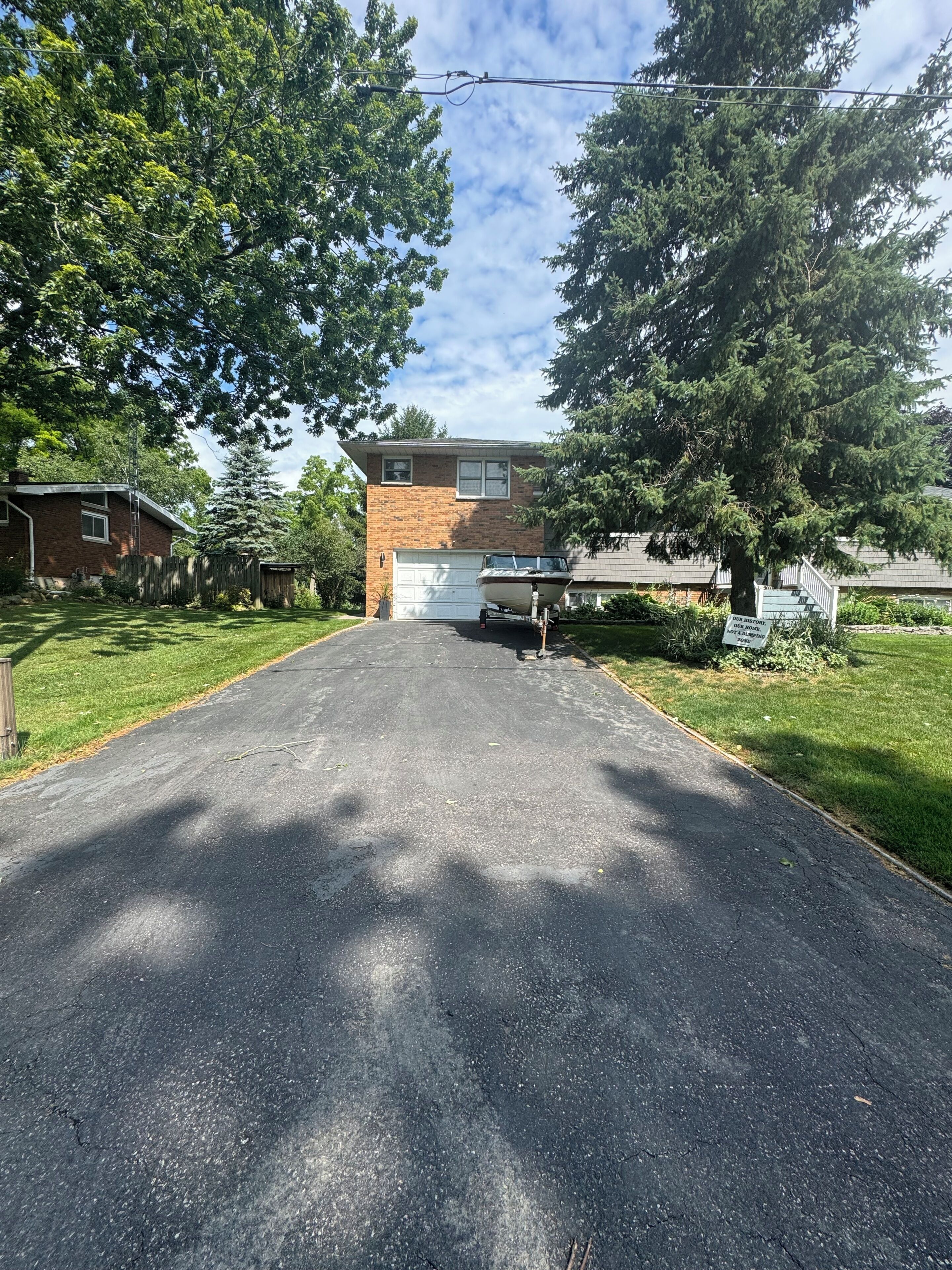 A residential driveway leading to a house with a garage, surrounded by trees and a clear sky.