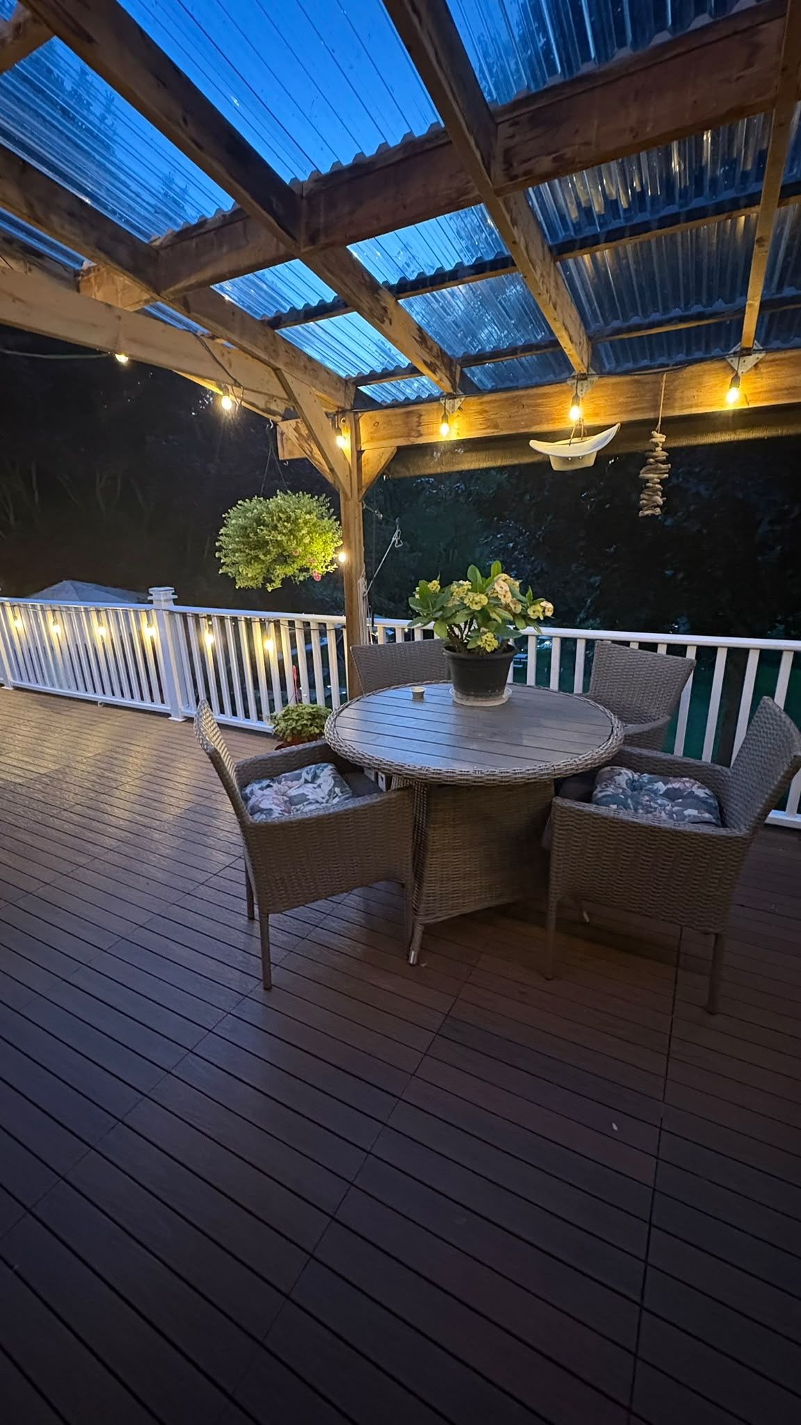 A covered outdoor deck with a round table and wicker chairs, surrounded by a white railing.