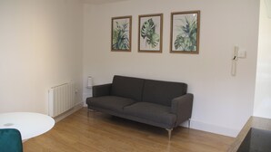 A living room with a grey sofa, a white round table, and three framed tropical leaf artworks on the wall. - East Street Haven - Modern Apartment in Colchester (Colchester)
