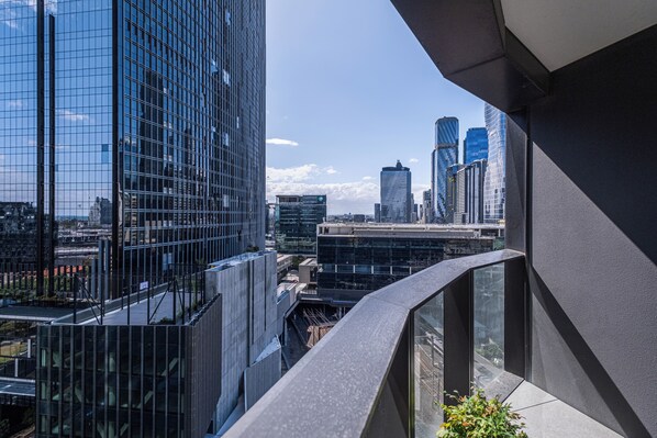 Un edificio alto con fachada de vidrio moderna, cielo despejado y paisaje urbano al fondo.