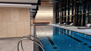 En inomhuspool med klart vatten, en metallstege och solstolar längs kanten.