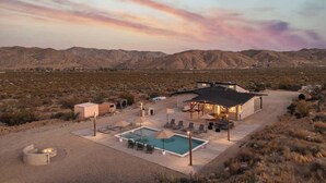 Un paysage désertique avec une maison moderne dotée d’une piscine, d’un espace salon extérieur et d’un coin barbecue.