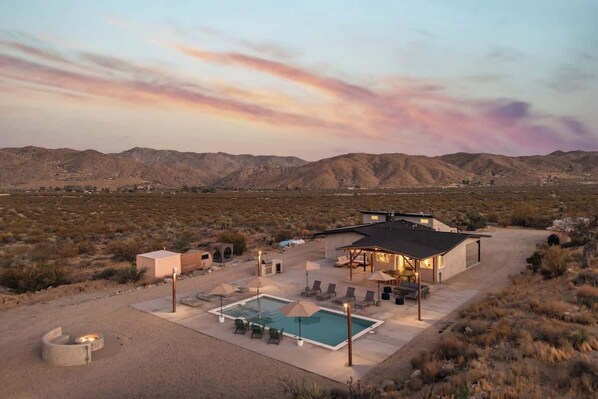Un paysage désertique avec une maison moderne dotée d’une piscine, d’un espace salon extérieur et d’un coin barbecue.