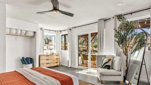 Une chambre à coucher moderne, avec un lit, une commode, une chaise et une grande fenêtre donnant sur l’extérieur.