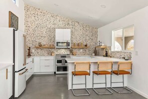 Une cuisine moderne avec des meubles blancs, un dosseret en granit et un îlot central doté de tabourets de bar.