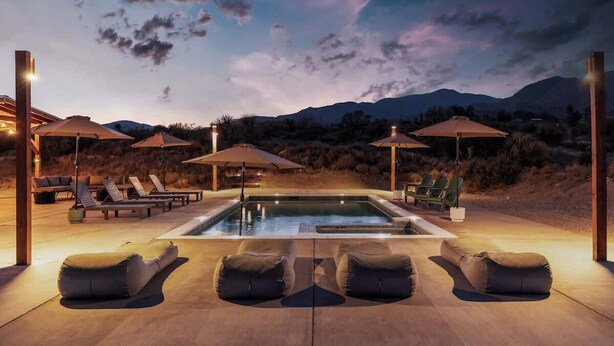 Un espace piscine doté de chaises longues et de parasols, entouré de montagnes.