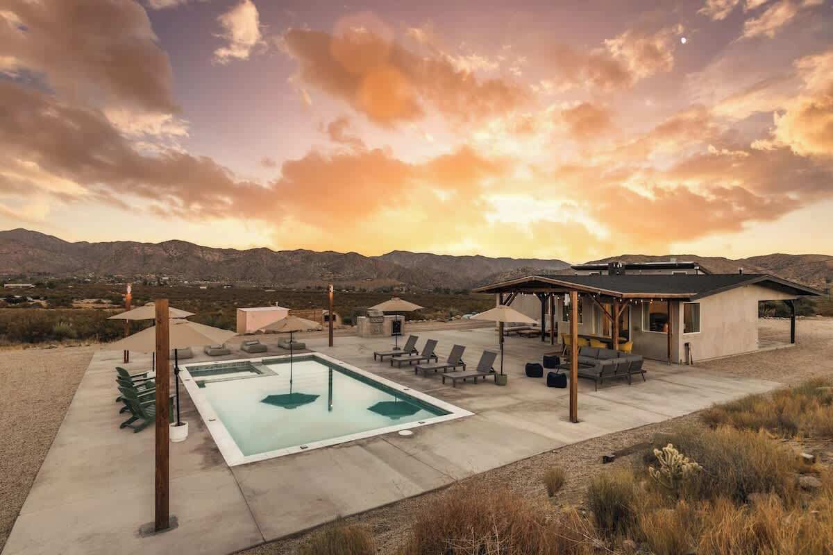 A pool area with lounge chairs and umbrellas, a covered seating area, and a view of mountains.
