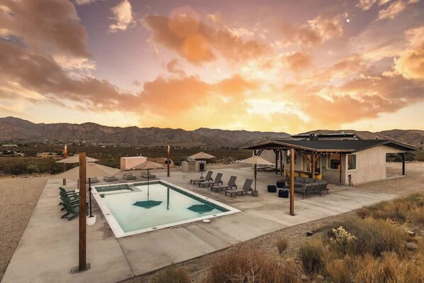 A pool area with lounge chairs and umbrellas, a covered seating area, and a view of mountains.