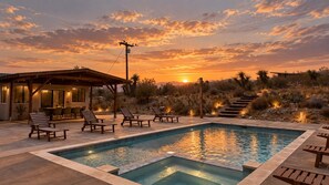 Ein Pool mit Liegestühlen, eine überdachte Terrasse und Blick auf den Sonnenuntergang.