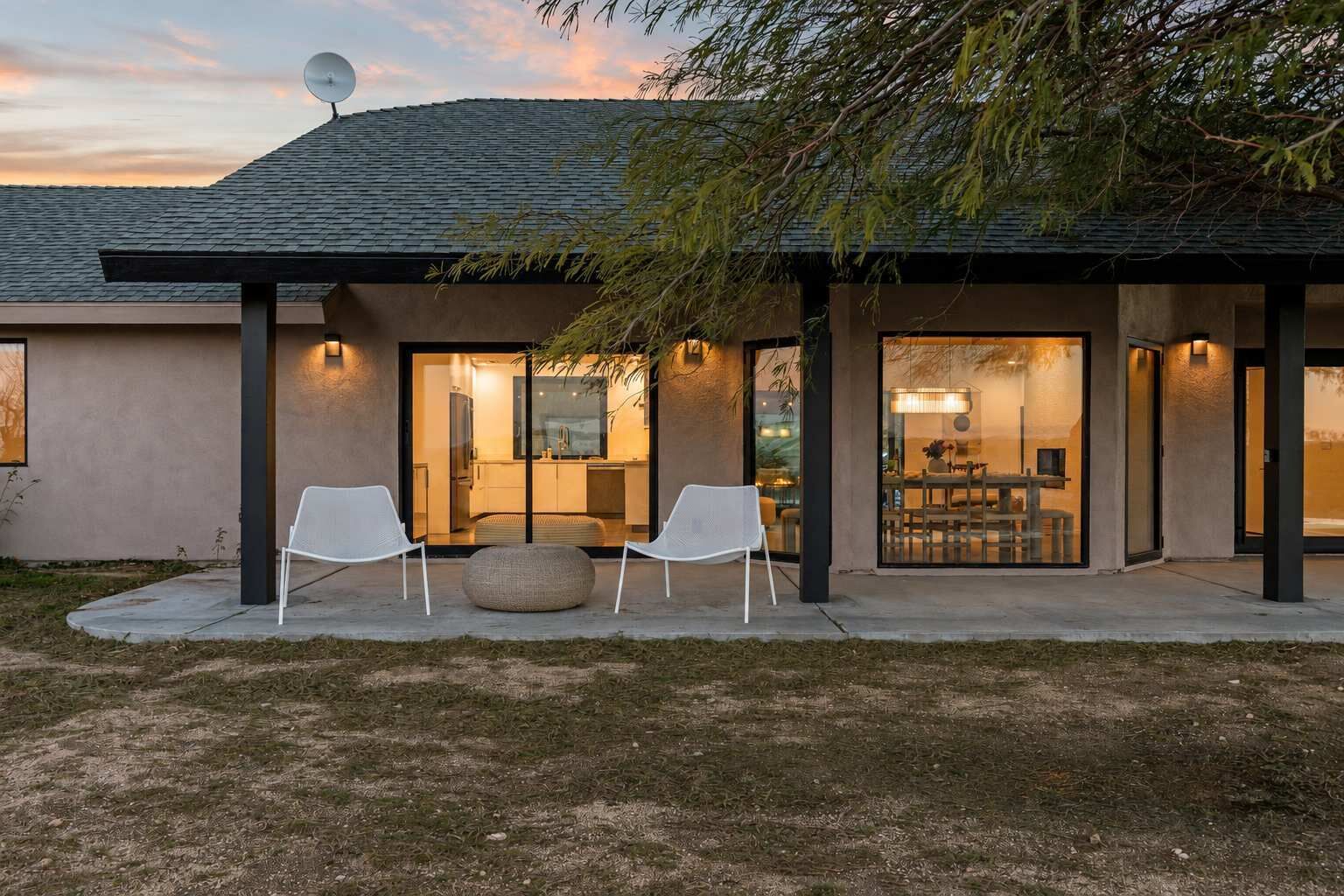 A modern house with a covered patio, two white chairs, and a dining area.