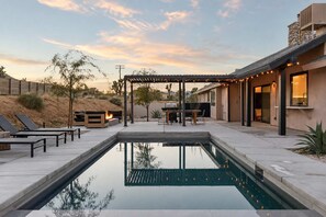 A swimming pool with lounge chairs and a barbecue area, surrounded by a patio and a covered seating area.