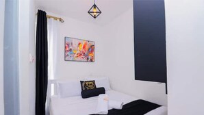 Una camera da letto con un letto, una combinazione di colori bianco e nero, un quadro appeso al muro e una lampada a sospensione.