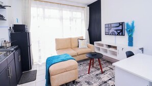Un soggiorno moderno con un divano, un tavolino, una TV e un angolo cottura con pensili e un frigorifero.