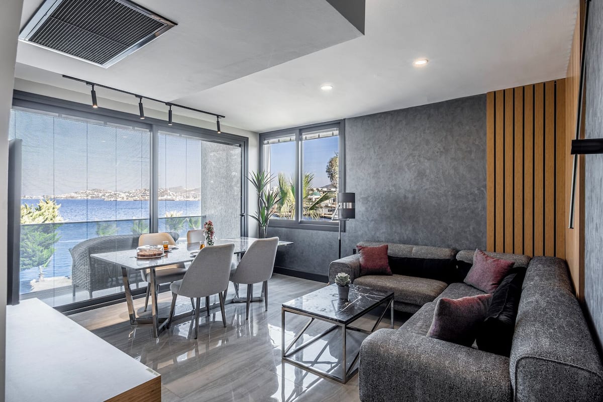 Un salon moderne avec une table basse en verre, un canapé gris et un coin repas comprenant une table et des chaises.