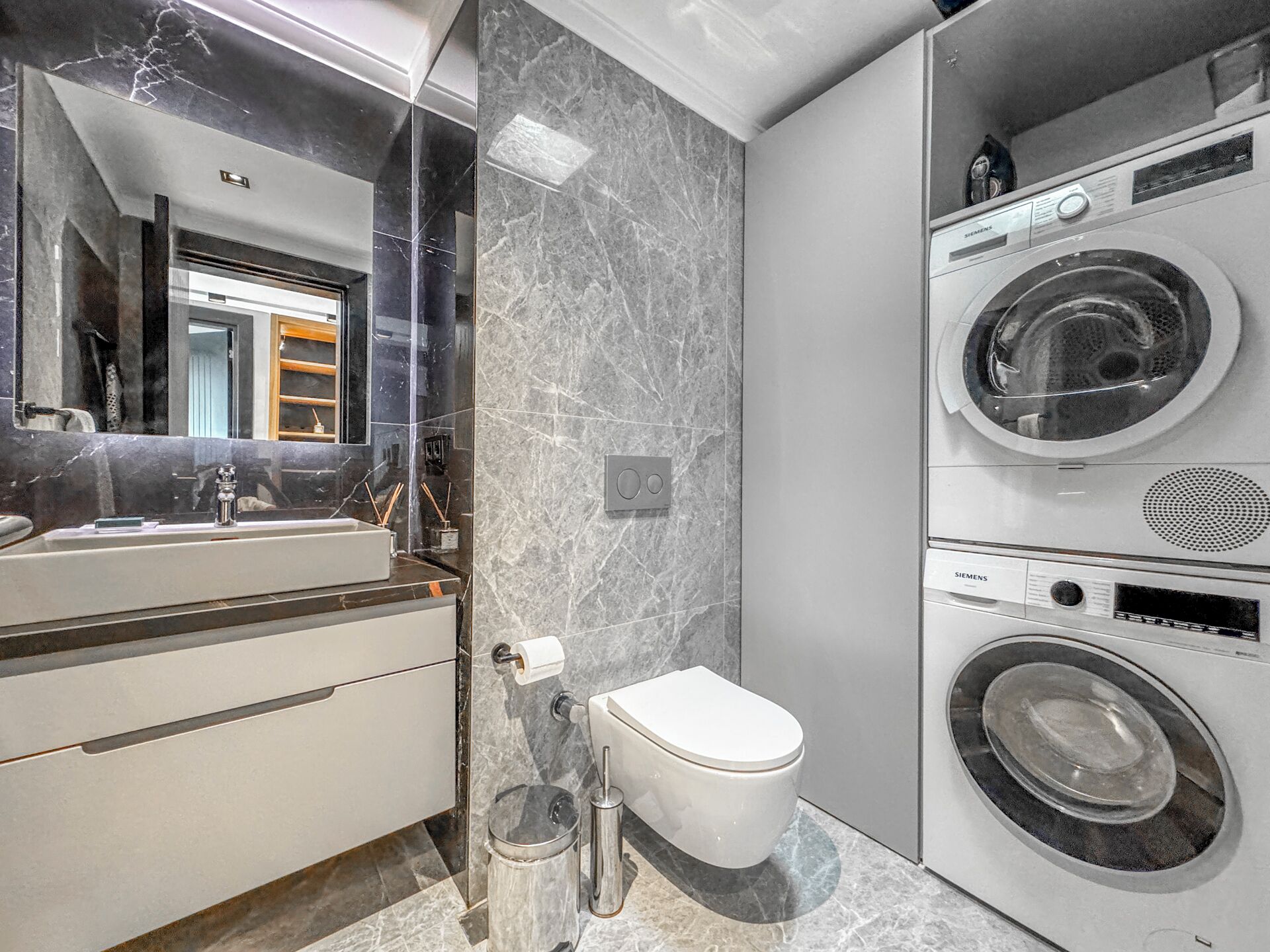 Un bagno moderno con un mobile lavabo in marmo, un water e una lavatrice e asciugatrice affiancate.