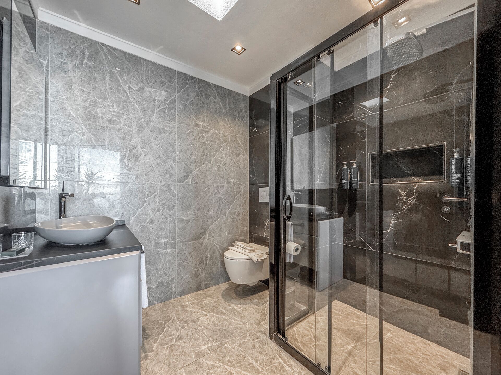 Une salle de bain moderne avec une douche à parois de verre, un lavabo sur colonne et des murs en marbre.
